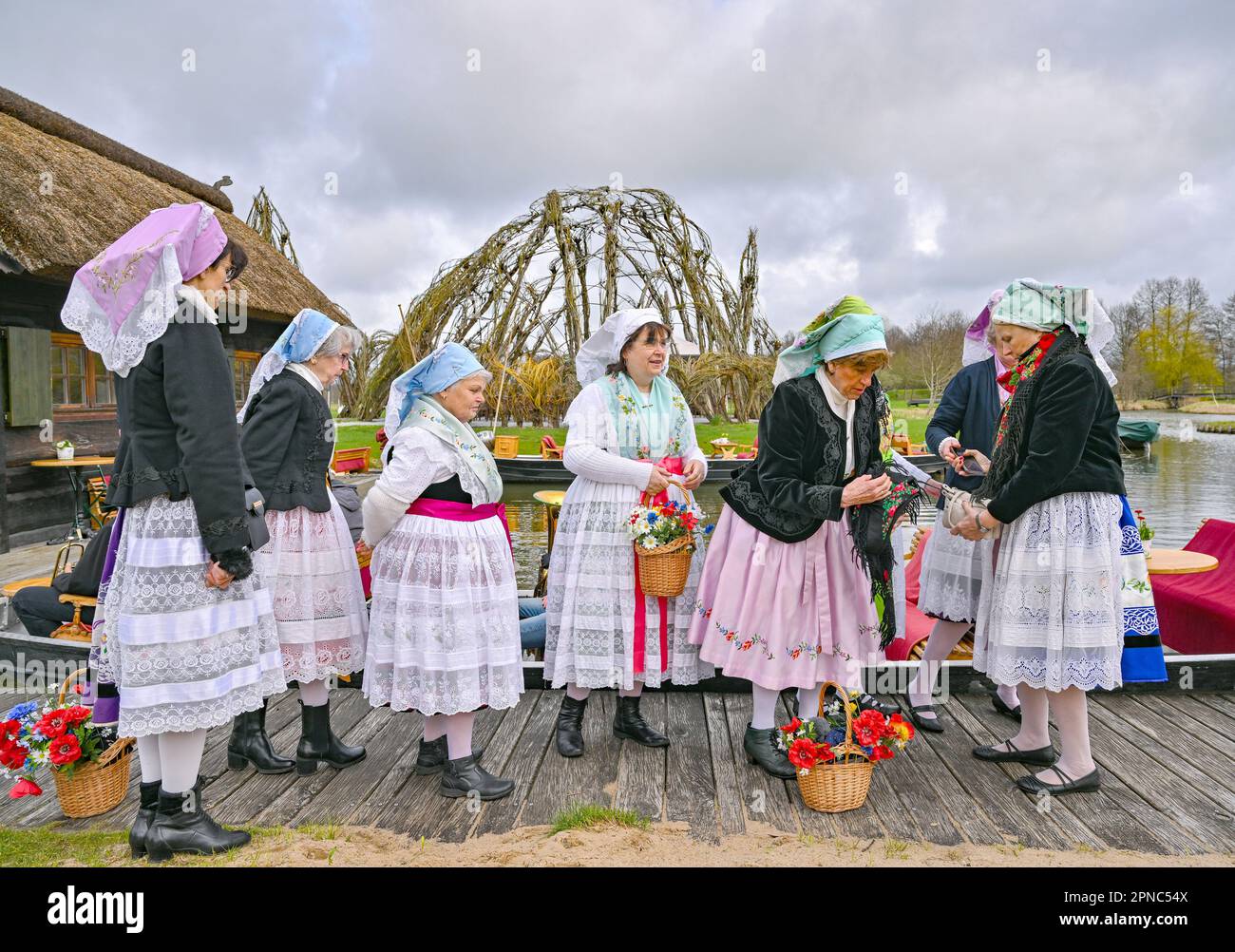 01 April 2023, Brandenburg, Schlepzig: Women in Sorbian-Wendish festive costumes wait for the season opening at the harbor at the Weidendom in the Spreewald village of Schlepzig. At the season opening, the pack (wooden pole for moving the barge) is ceremoniously handed over to a bargeman. At the same time in several places in the Spreewald, the traditional opening of the season with the handing over of the pack took place. Photo: Patrick Pleul/dpa Stock Photo