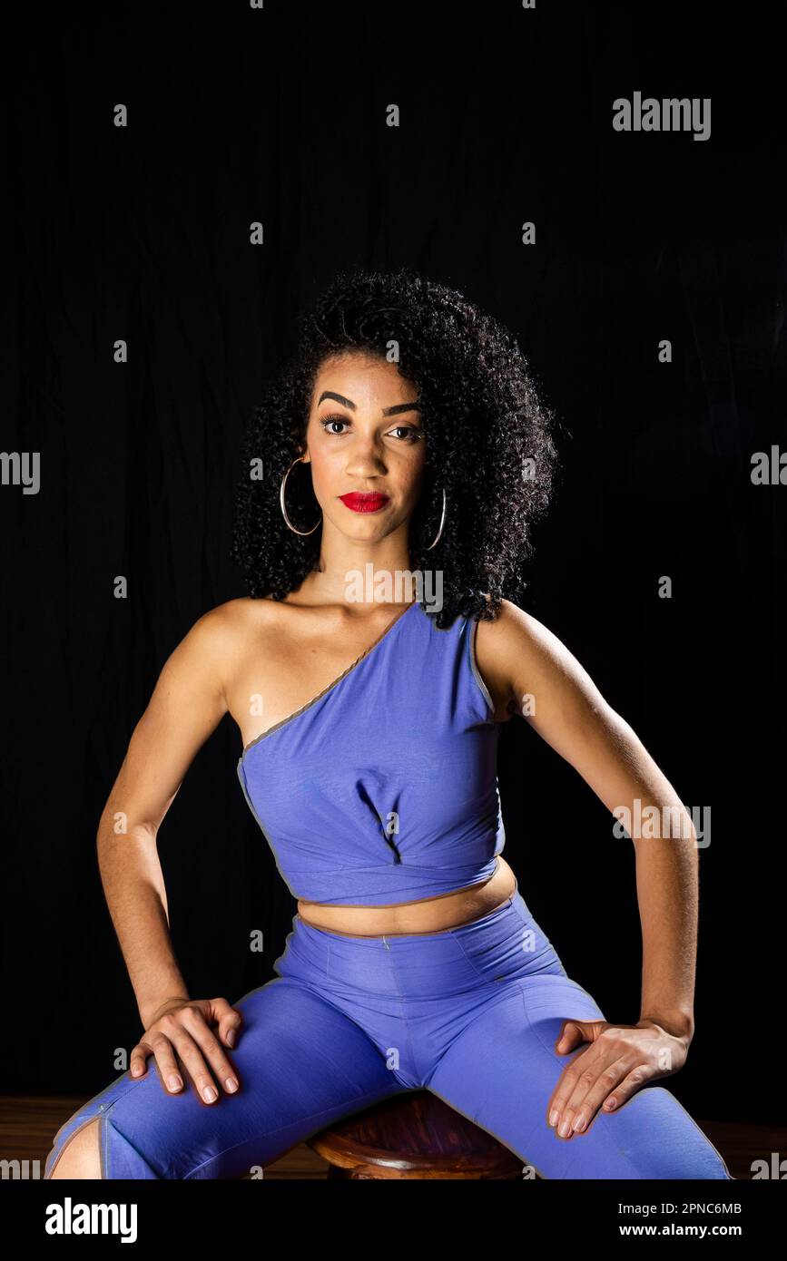 Young woman wearing blue outfit sitting on a wooden stool. Isolated ...