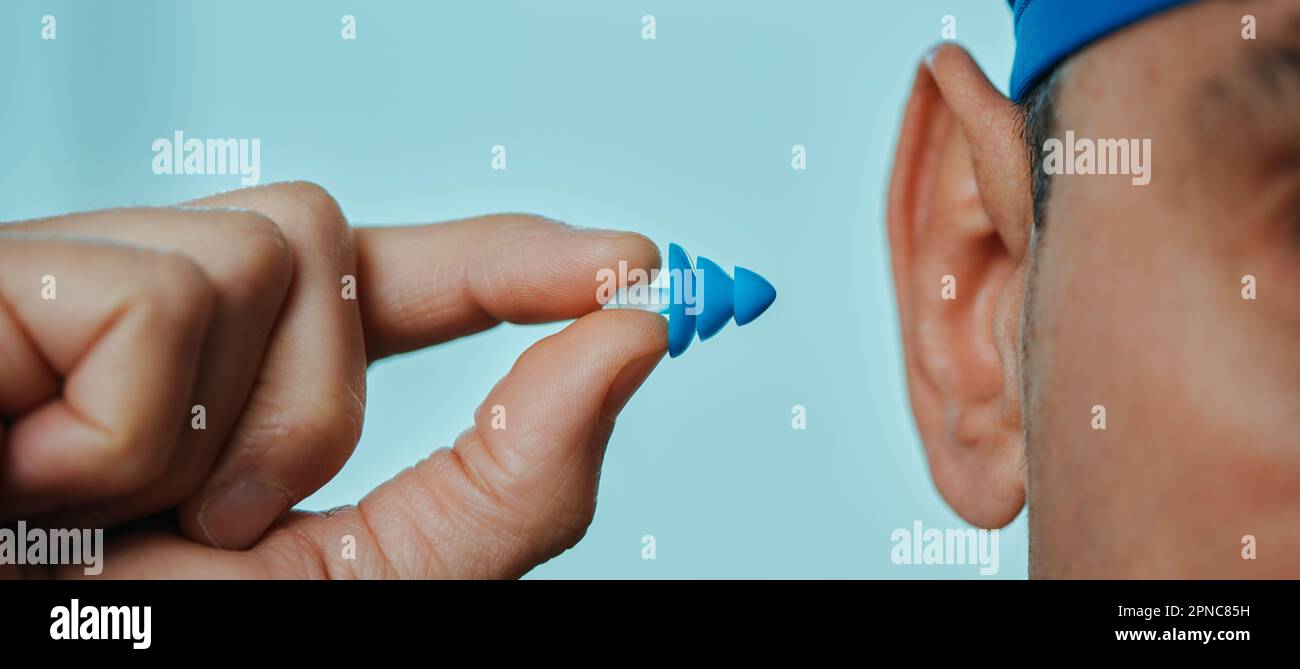 a swimmer man, wearing a blue swimming cap, is about to put an earplug, in a swimming pool, in a panoramic format to use as web banner or header Stock Photo