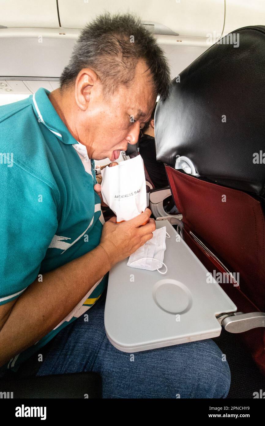 Asian man feeling motion sickness vomiting into air sickness bag in