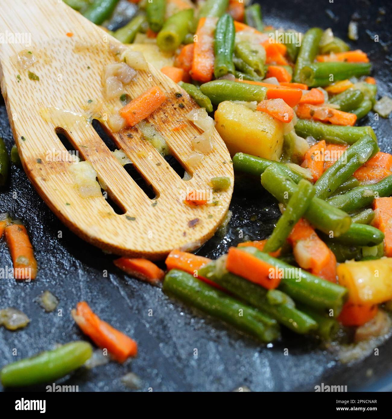 A wooden spoon stirring a mixture of green beans and carrots in a ceramic bowl Stock Photo