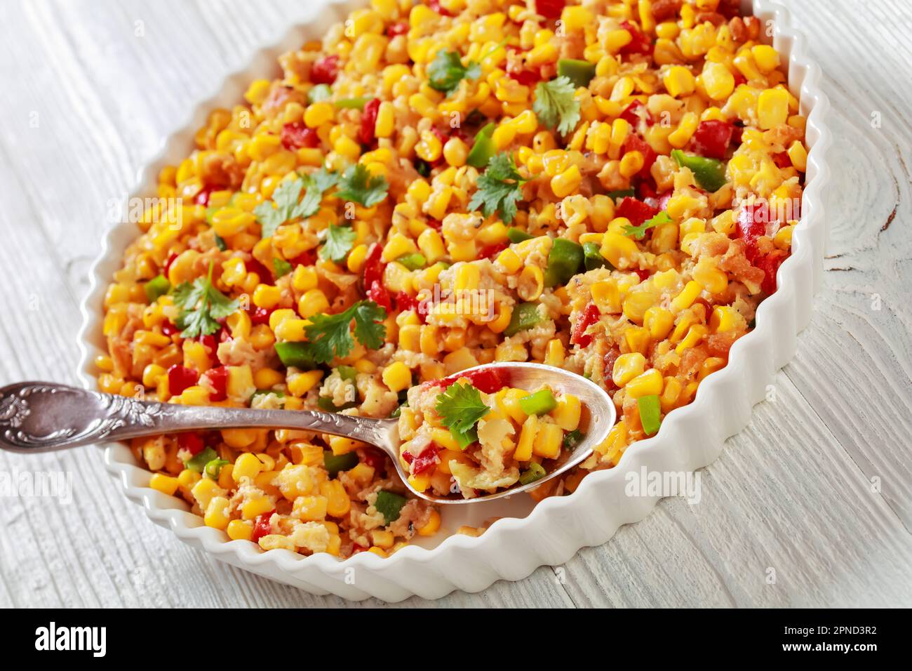 Corn casserole with sweet red pepper, butter, crackers and eggs in baking dish with spoon on