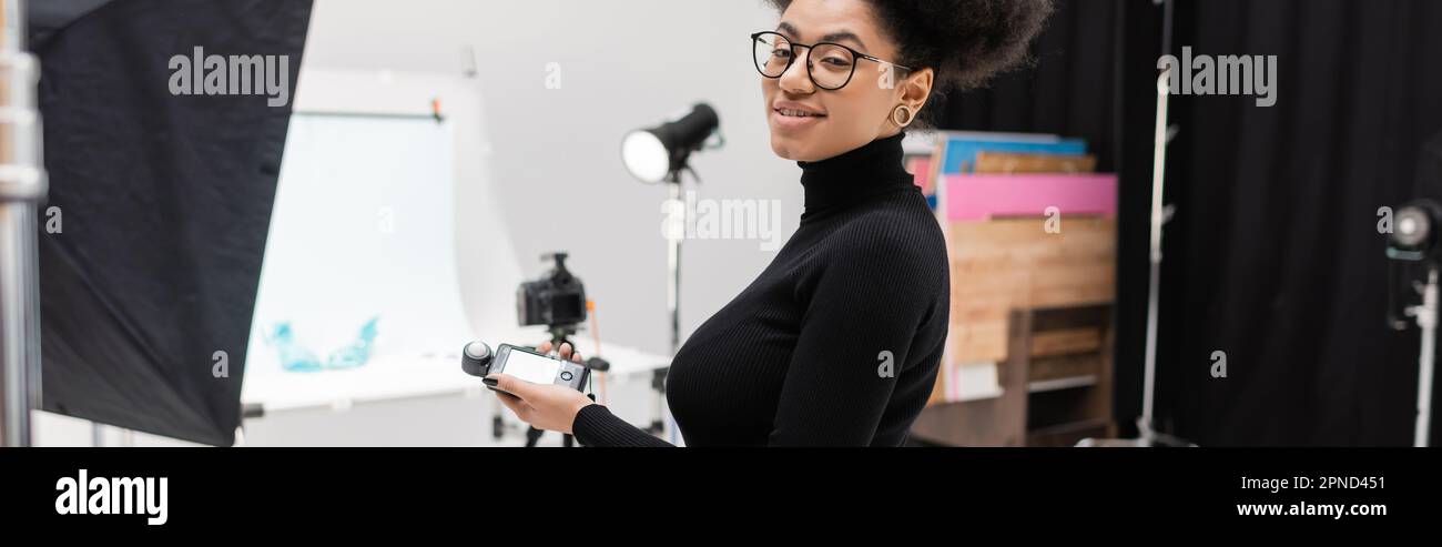 positive african american content maker in eyeglasses holding exposure  meter and smiling at camera in photo studio, banner,stock image Stock Photo  - Alamy