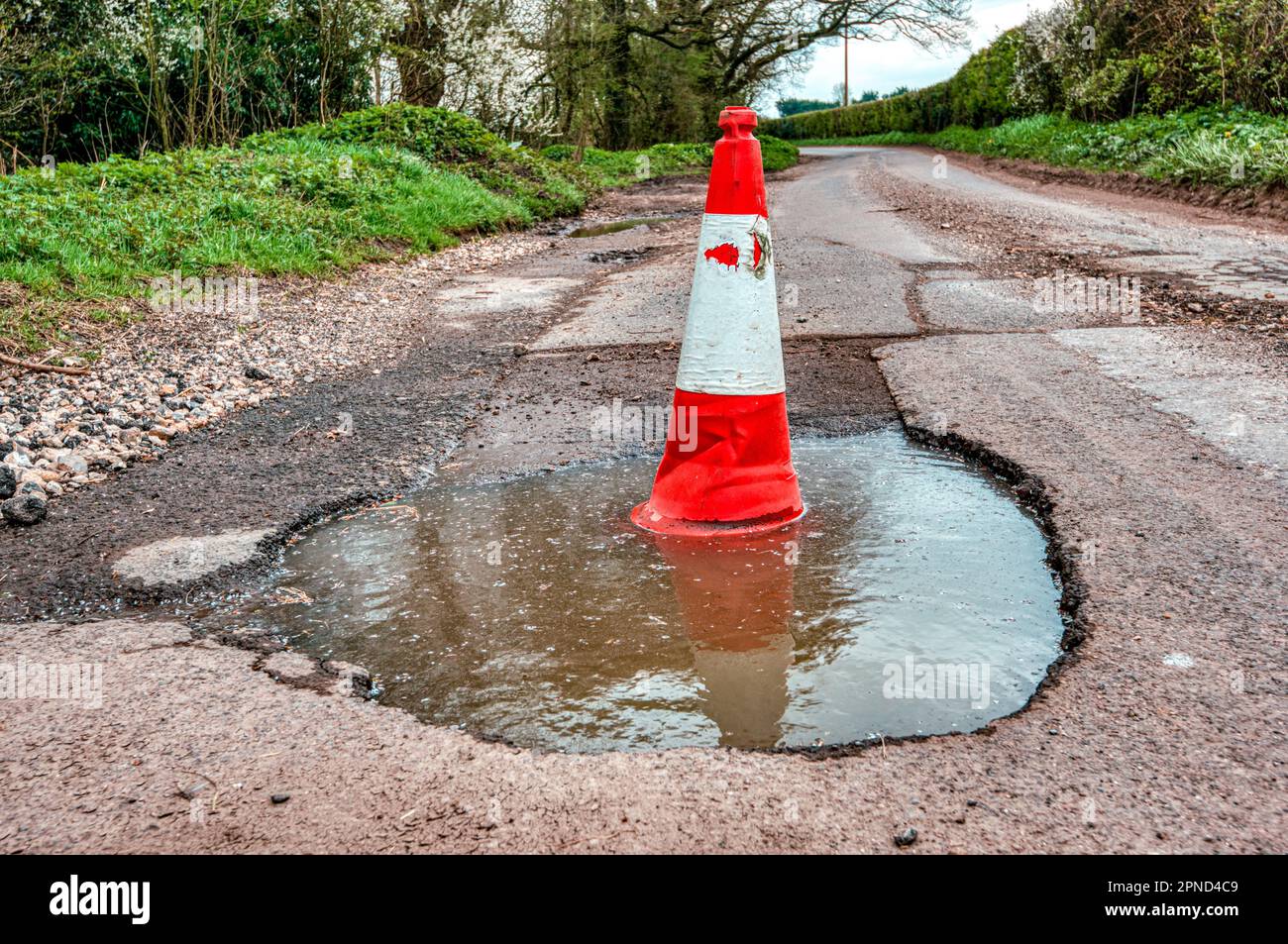 Giant pothole with a traffic cone sitting inside, Battle Corner, Upper Wield, Alresford, Hampshire UK Stock Photo