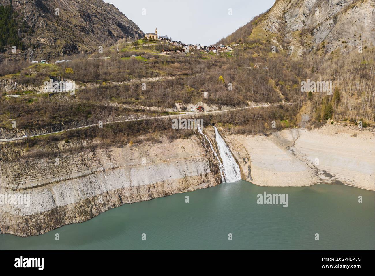 Panoramic drone shot of the waterfall flowing into Lac Chambon and the village of Mizoën in French Alps Stock Photo