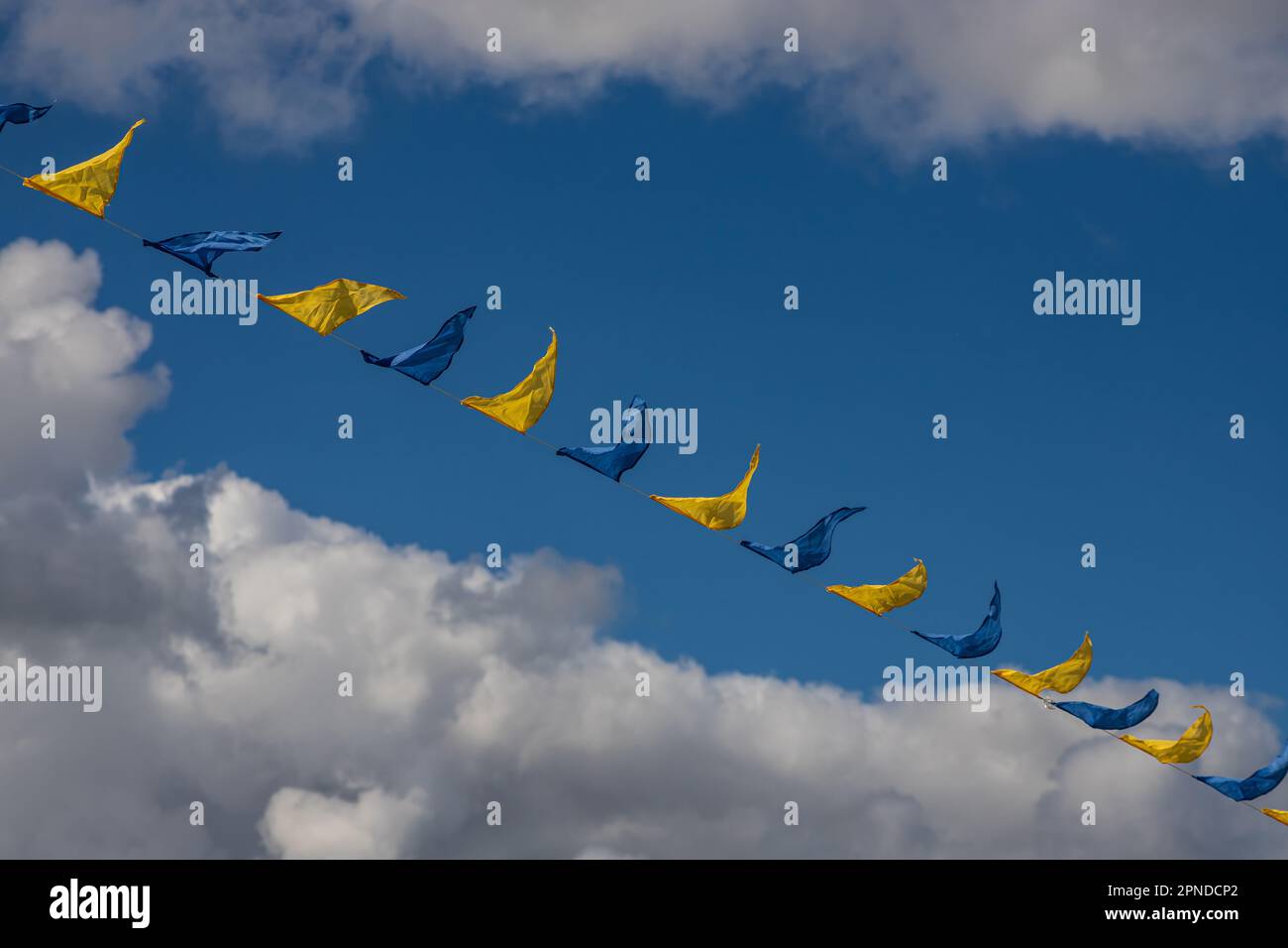 Yellow and blue triangular festival flags on sky background with white clouds. Outdoor Celebration Party. Festive mood Stock Photo