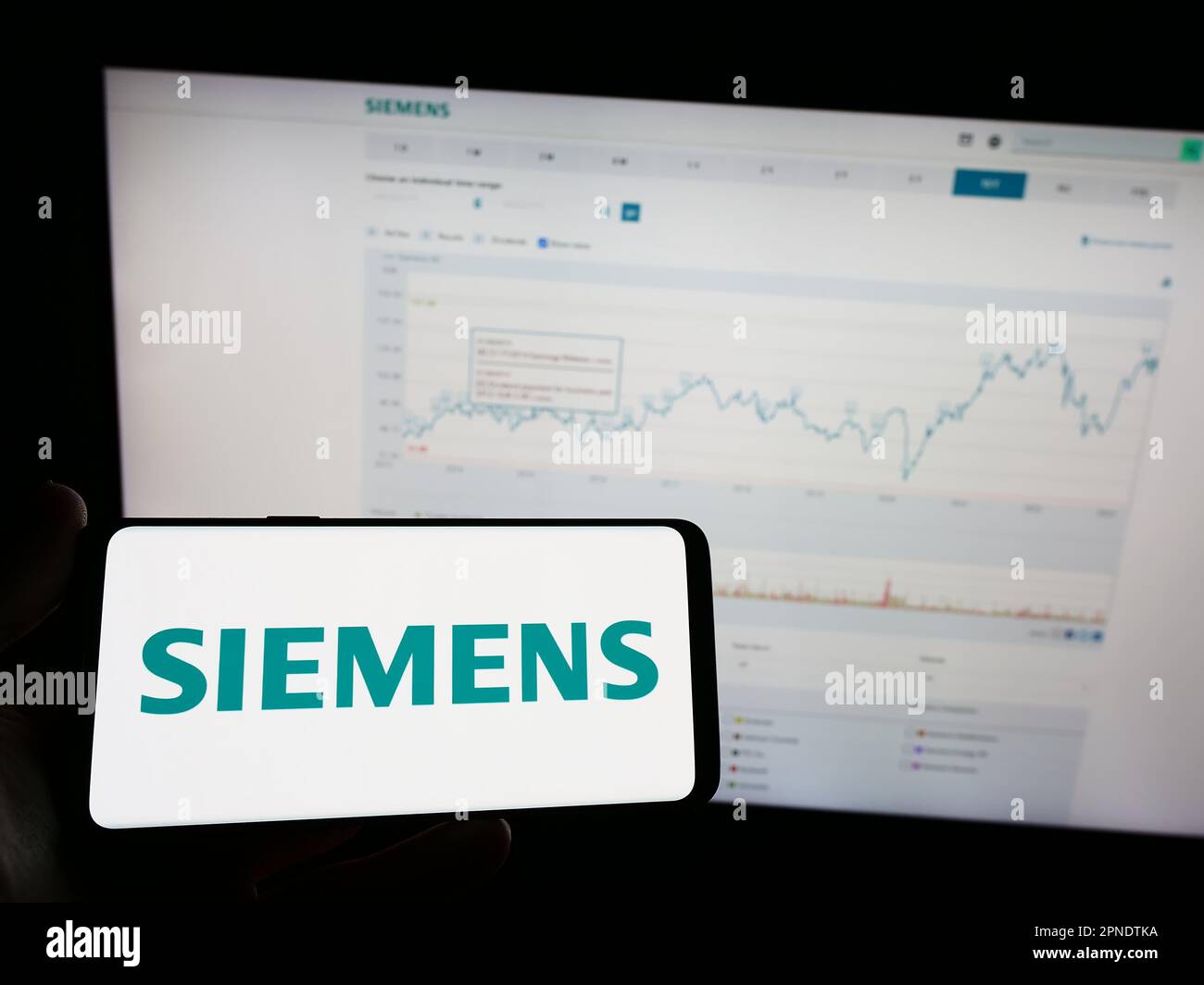 Person holding mobile phone with logo of German conglomerate Siemens AG on screen in front of business web page. Focus on phone display. Stock Photo
