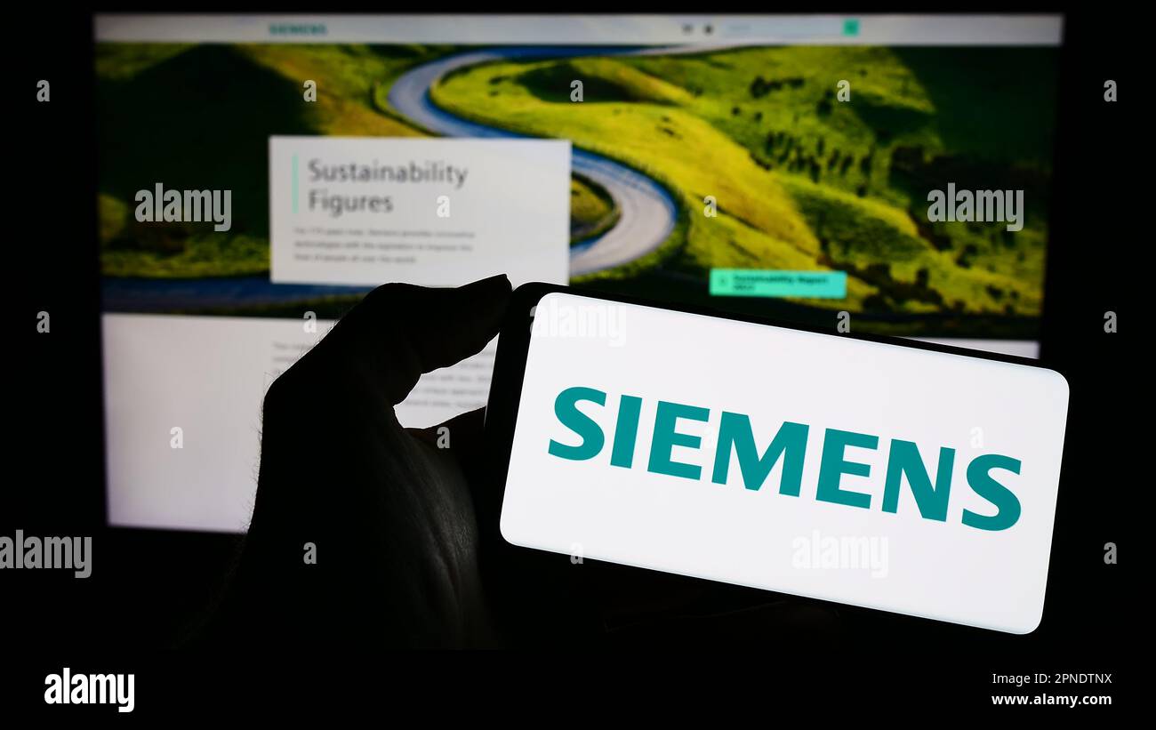 Person holding cellphone with logo of German conglomerate Siemens AG on screen in front of business webpage. Focus on phone display. Stock Photo