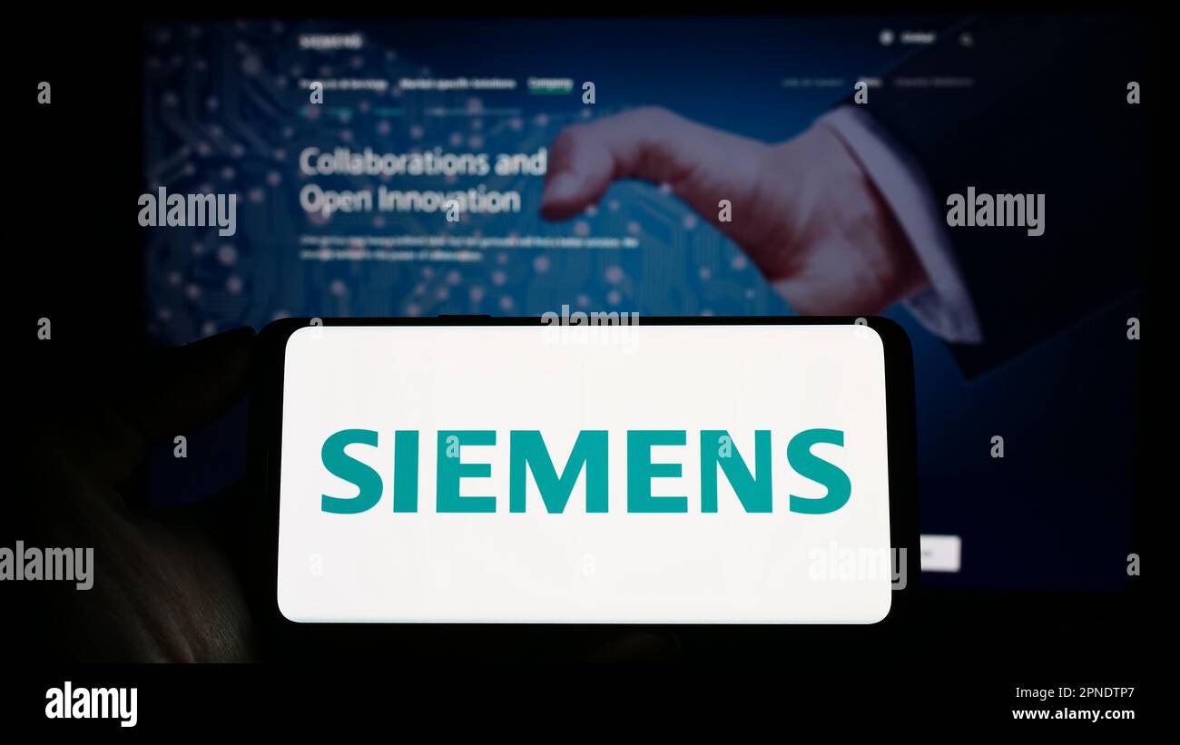 Person holding smartphone with logo of German conglomerate Siemens AG on screen in front of website. Focus on phone display. Stock Photo