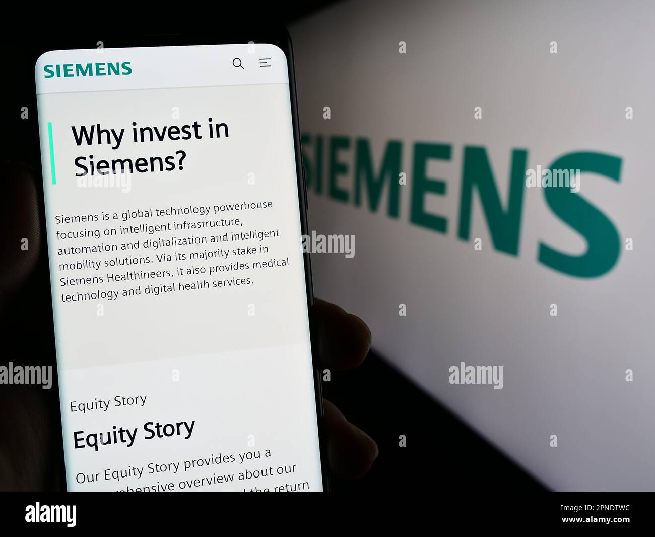 Person holding smartphone with web page of German conglomerate Siemens AG on screen in front of business logo. Focus on center of phone display. Stock Photo