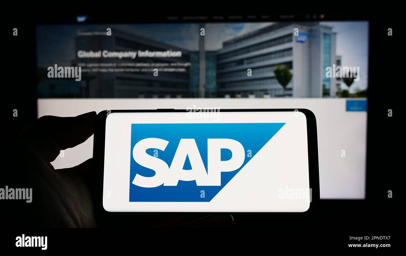 person holding smartphone with logo of german software company sap se on screen in front of website focus on phone display 2PNDTX7