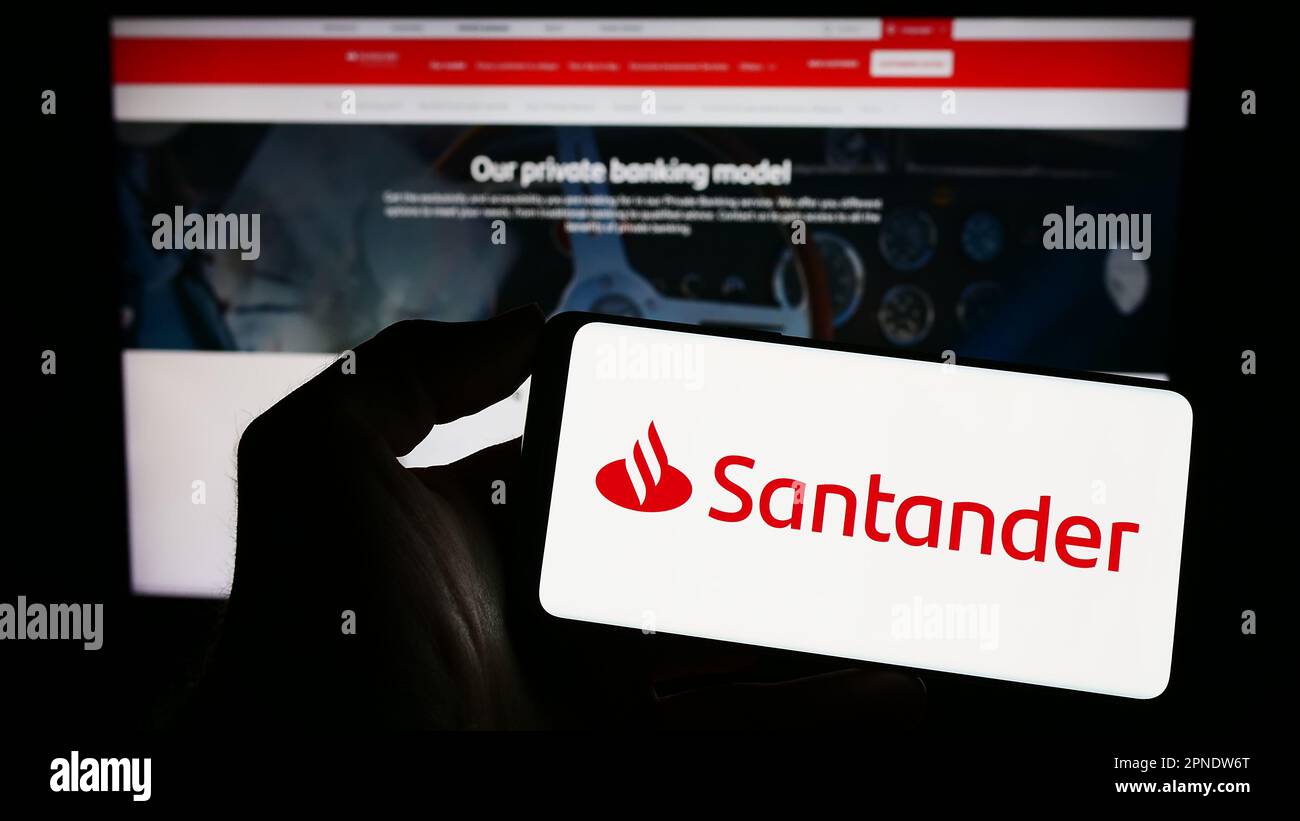 Person holding smartphone with logo of Spanish banking company Banco Santander S.A. on screen in front of website. Focus on phone display. Stock Photo