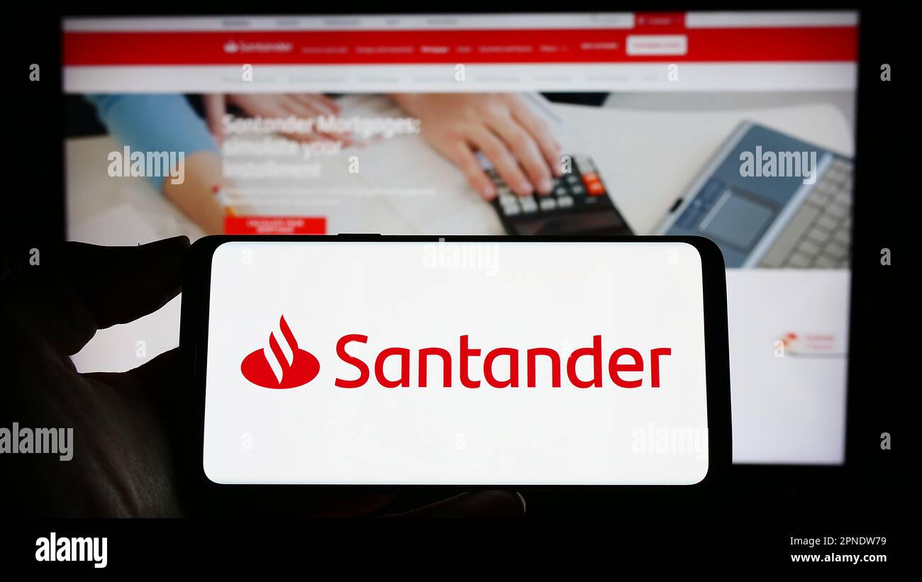 Person holding cellphone with logo of Spanish banking company Banco Santander SA on screen in front of business webpage. Focus on phone display. Stock Photo
