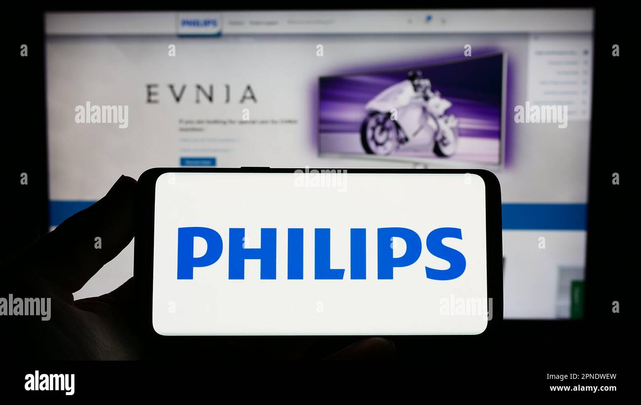 Person holding smartphone with logo of Dutch company Koninklijke Philips N.V. on screen in front of website. Focus on phone display. Stock Photo