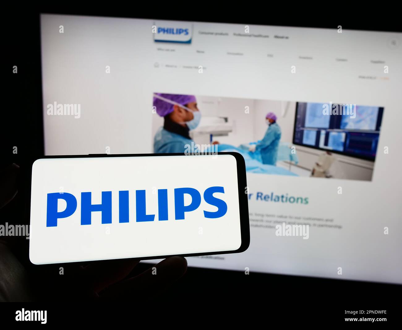 Person holding mobile phone with logo of Dutch company Koninklijke Philips N.V. on screen in front of business web page. Focus on phone display. Stock Photo
