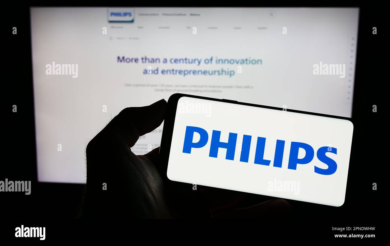 Person holding cellphone with logo of Dutch company Koninklijke Philips NV on screen in front of business webpage. Focus on phone display. Stock Photo