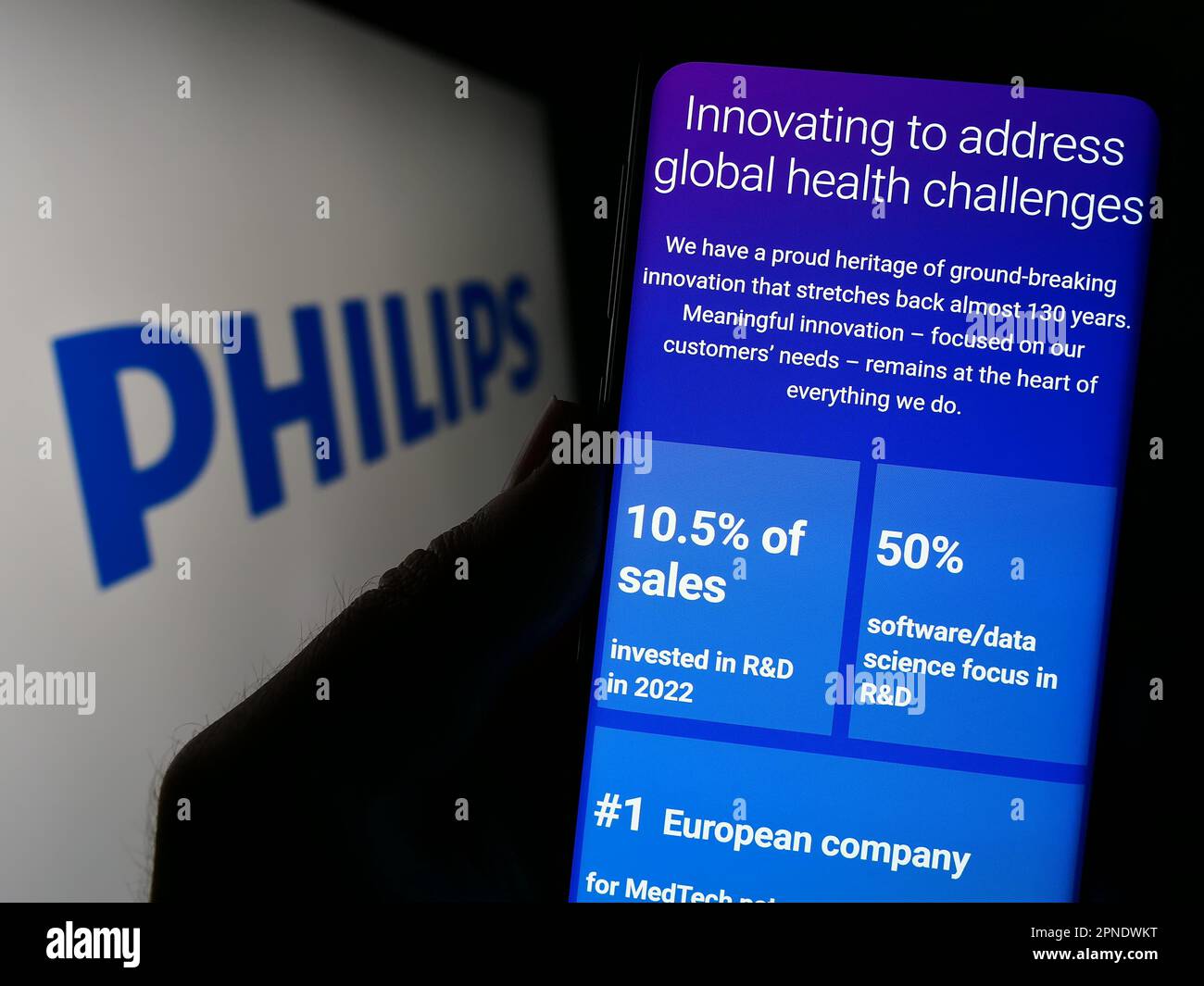 Person holding cellphone with webpage of Dutch company Koninklijke Philips NV on screen in front of logo. Focus on center of phone display. Stock Photo