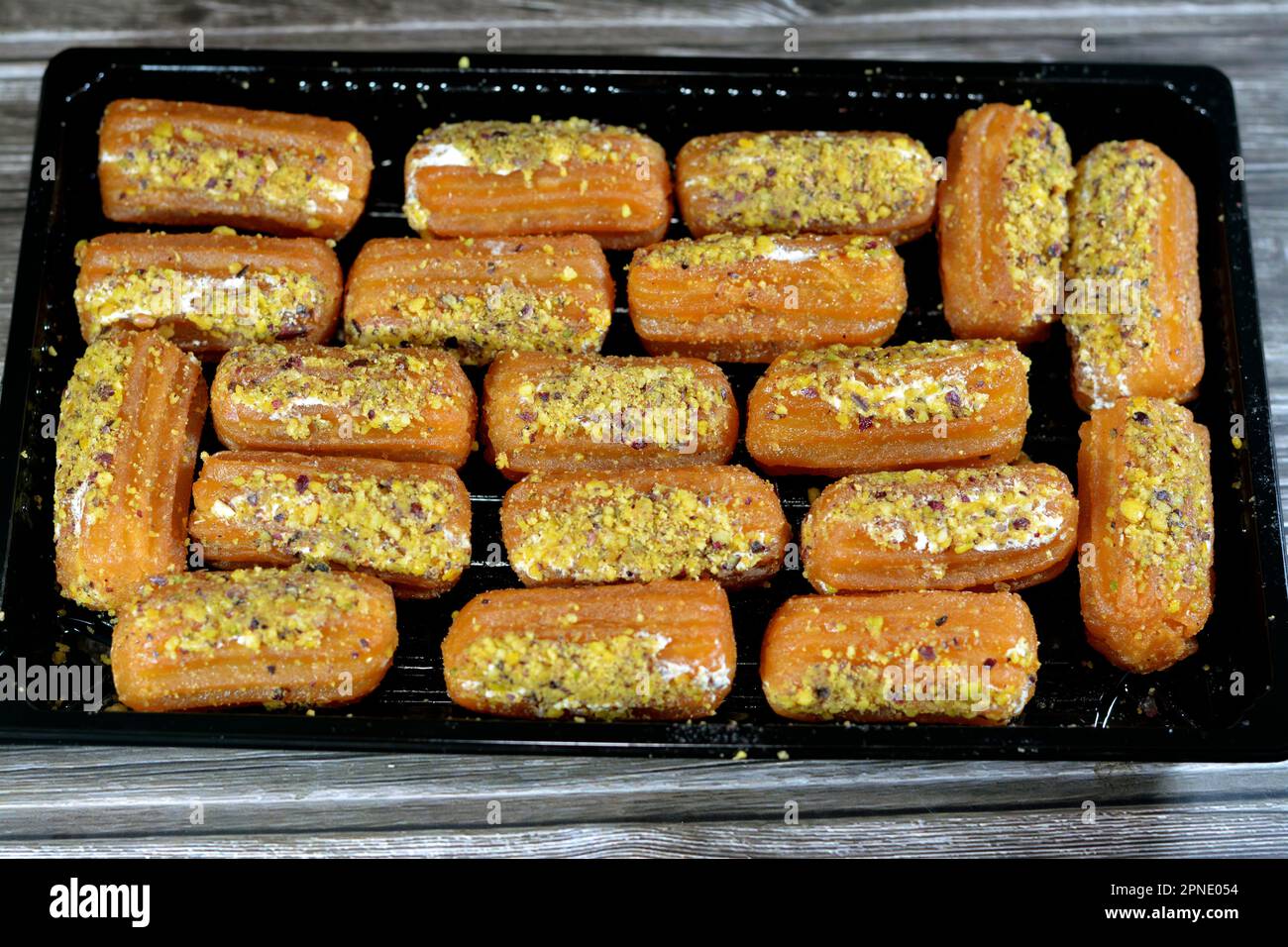 Tulumba, Bamiyeh or Balah El Sham stuffued with whipped cream and covered with pistachios and nuts, deep fried batter dessert soaked in syrup, similar Stock Photo