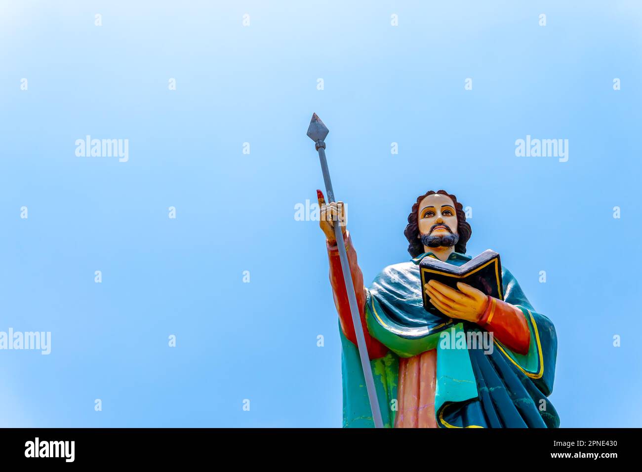 Status of Jesus with a spade or stick in one hand and a book or bible in his other hand with clear blue sky in the background Stock Photo