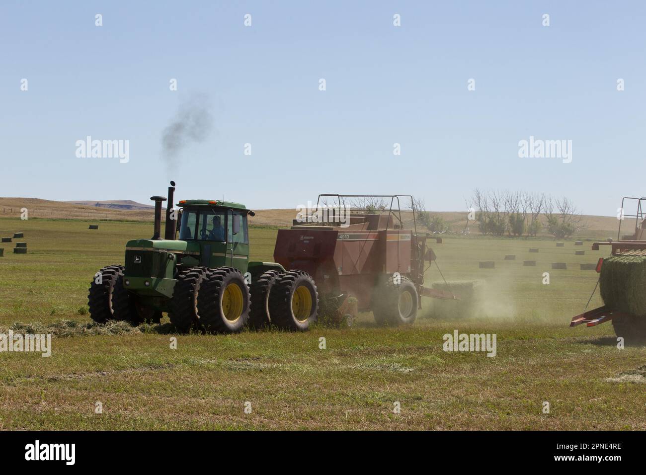 A bale pops out of one baler as another baler goes the opposite direction down windrows of alfalfa in an irrigated field, near Augusta, MT. Stock Photo