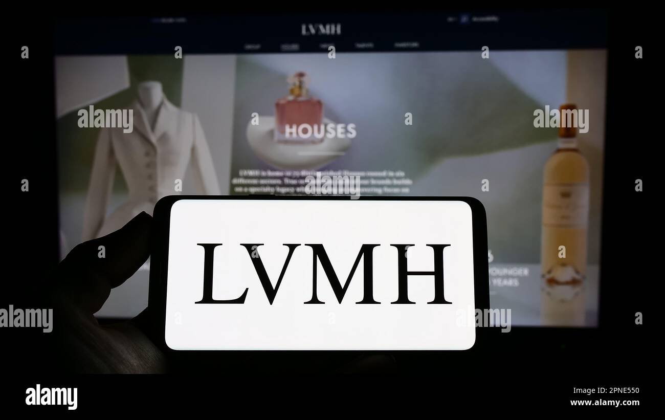 Person holding smartphone with logo of company LVMH Moet Hennessy Louis Vuitton SE on screen in front of website. Focus on phone display. Stock Photo