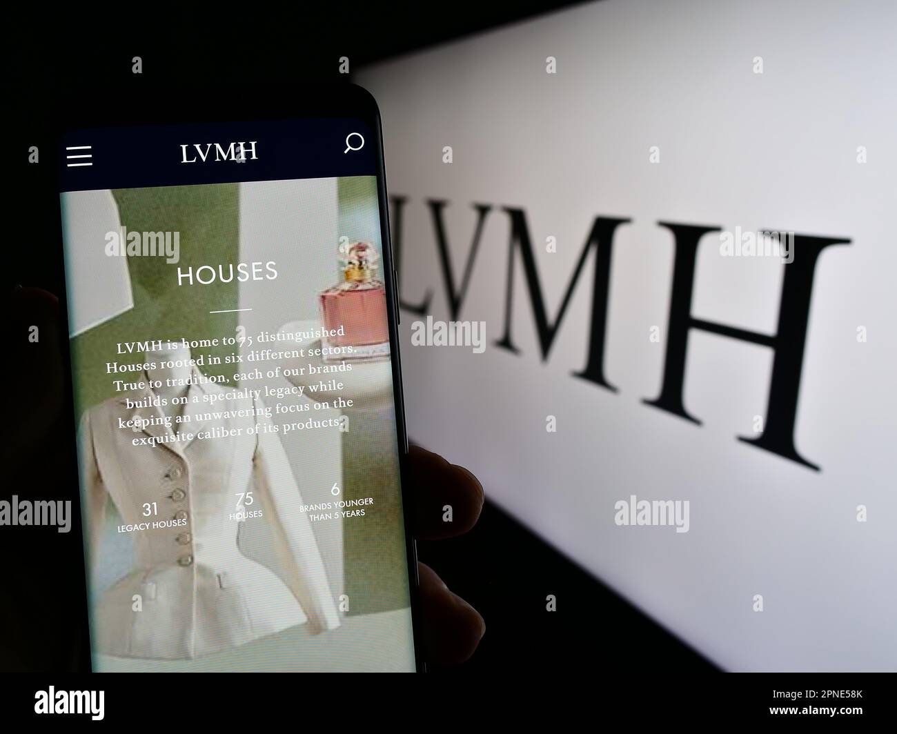 Person holding cellphone with webpage of company LVMH Moet Hennessy Louis Vuitton SE on screen in front of logo. Focus on center of phone display. Stock Photo