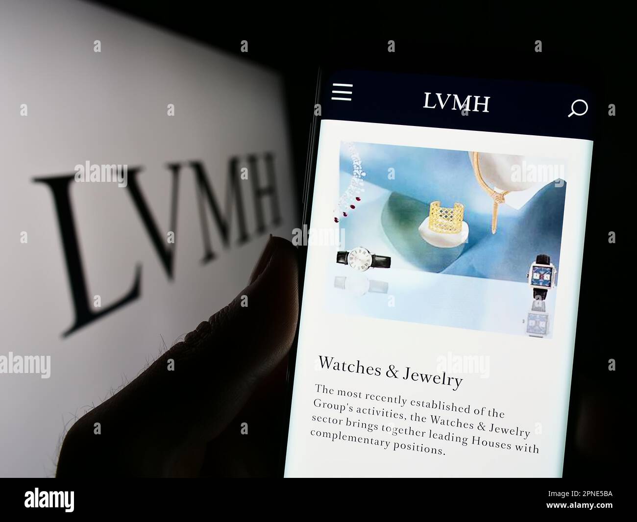Person holding smartphone with web page of company LVMH Moet Hennessy Louis Vuitton SE on screen with logo. Focus on center of phone display. Stock Photo