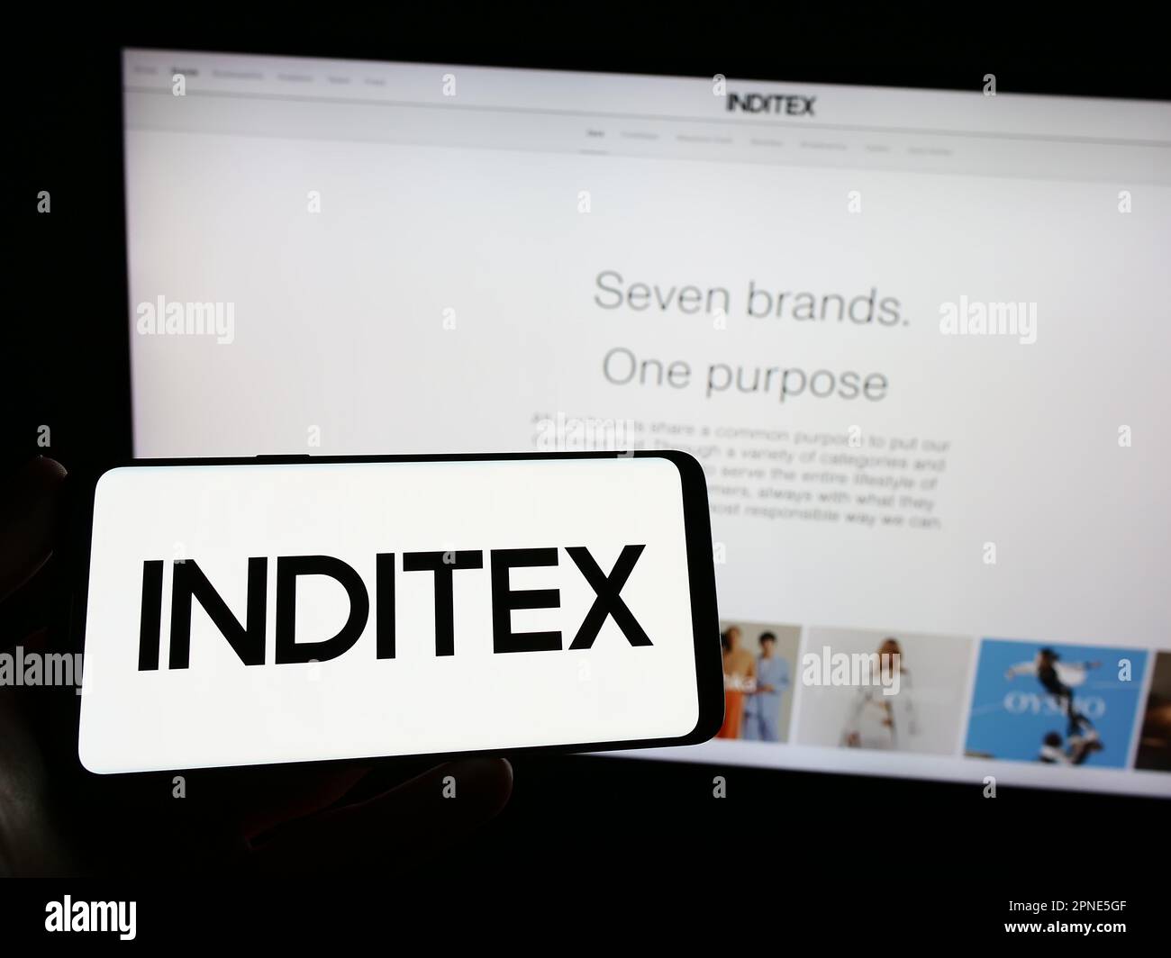 Person holding smartphone with logo of Industria de Diseno Textil S.A. (Inditex) on screen in front of website. Focus on phone display. Stock Photo