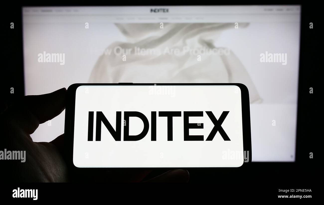 Person holding cellphone with logo of Industria de Diseno Textil S.A. (Inditex) on screen in front of business webpage. Focus on phone display. Stock Photo