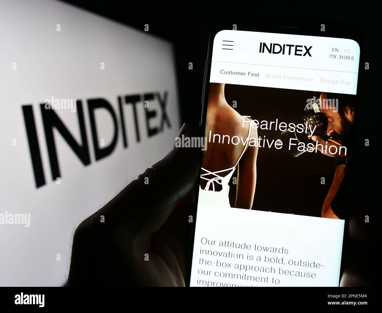 Person holding cellphone with webpage of Industria de Diseno Textil S.A. (Inditex) on screen in front of logo. Focus on center of phone display. Stock Photo