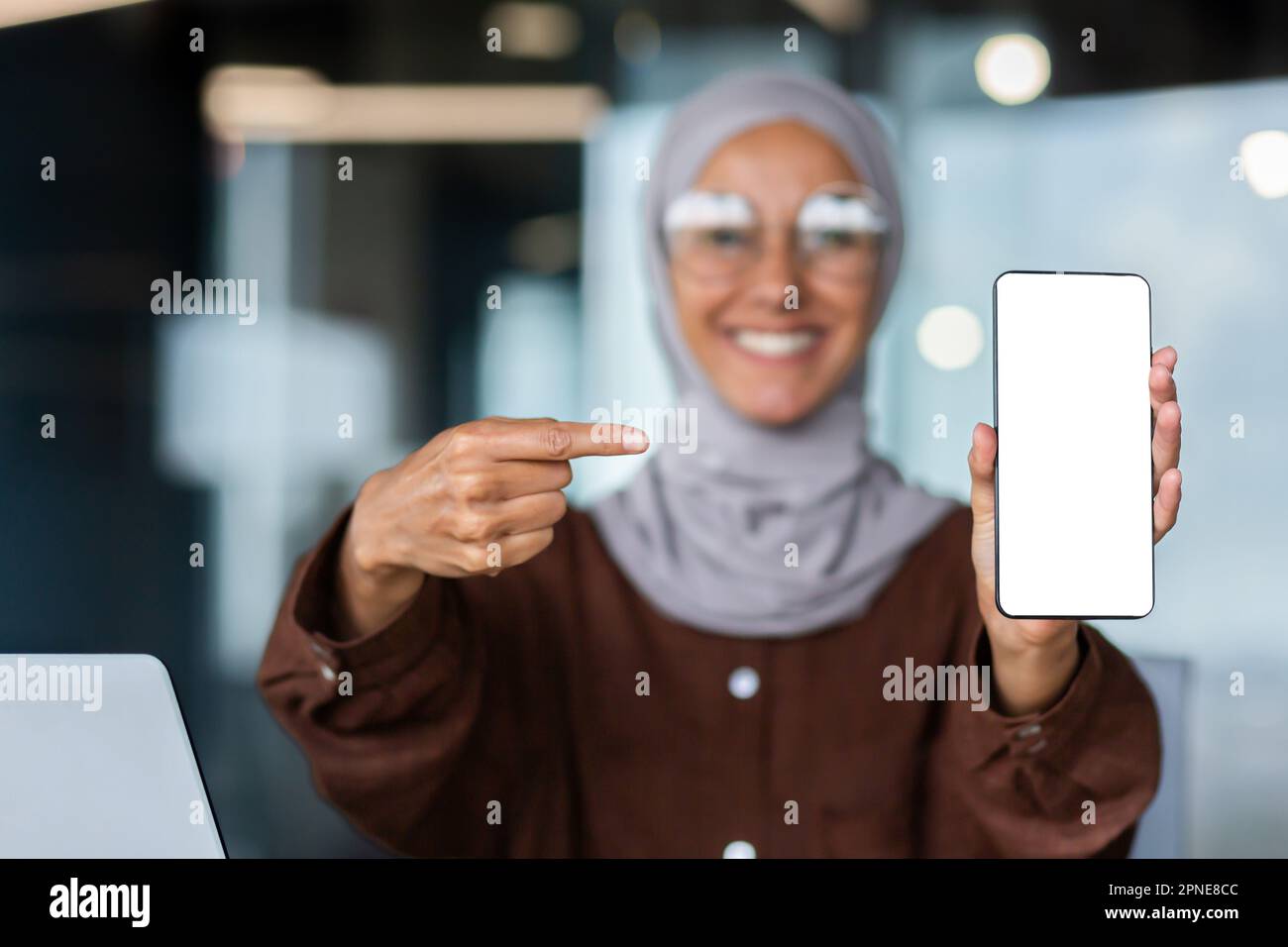 A young woman in a hijab in a blurred background is holding a phone in ...