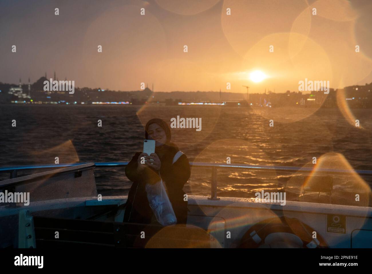Eminonu, Istanbul, Turkey. 18th Apr, 2023. A woman takes a selfies with their mobile phone at sunset while traveling by ferry across the Bosphorus in Istanbul on a rainy day. (Credit Image: © Tolga Uluturk/ZUMA Press Wire) EDITORIAL USAGE ONLY! Not for Commercial USAGE! Stock Photo