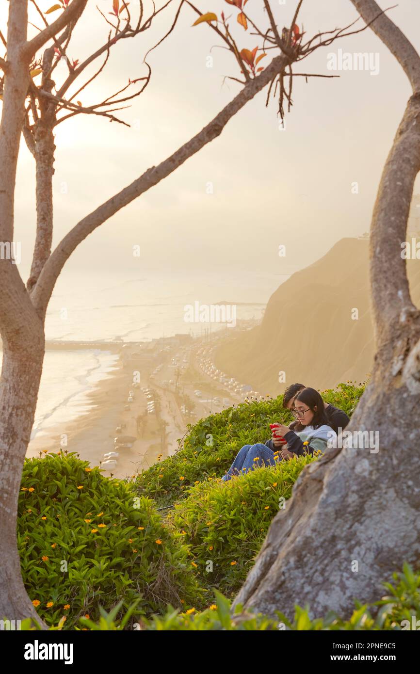 A couple sitting in front of the Lima Malecon cliffs at sunset ...