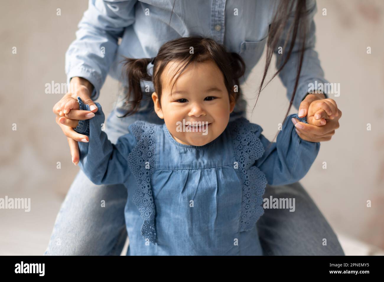 Japanese Baby Girl Holding Mom's Hands Learning To Walk Indoors Stock Photo