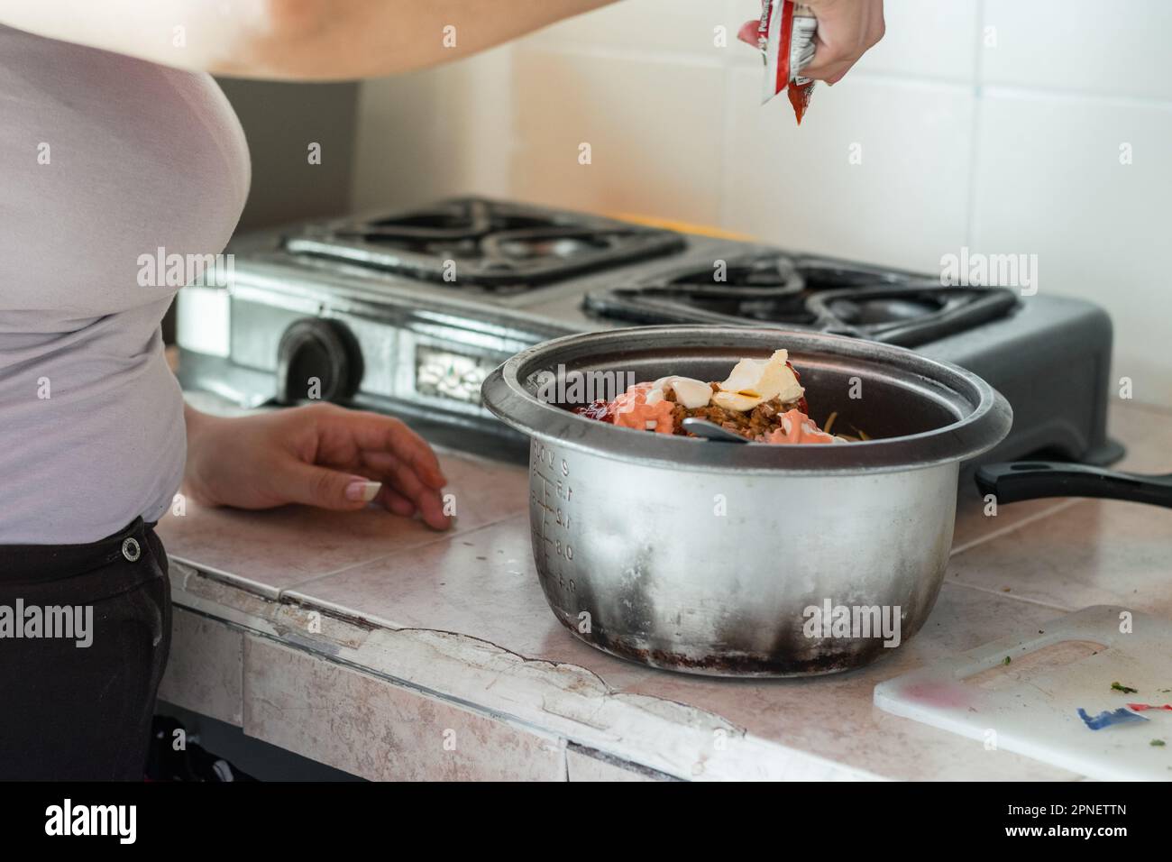 latin woman preparing food. pouring sauce over food to stir it Stock Photo