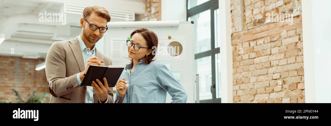 Smiling two colleagues looking at notepad in the office Stock Photo