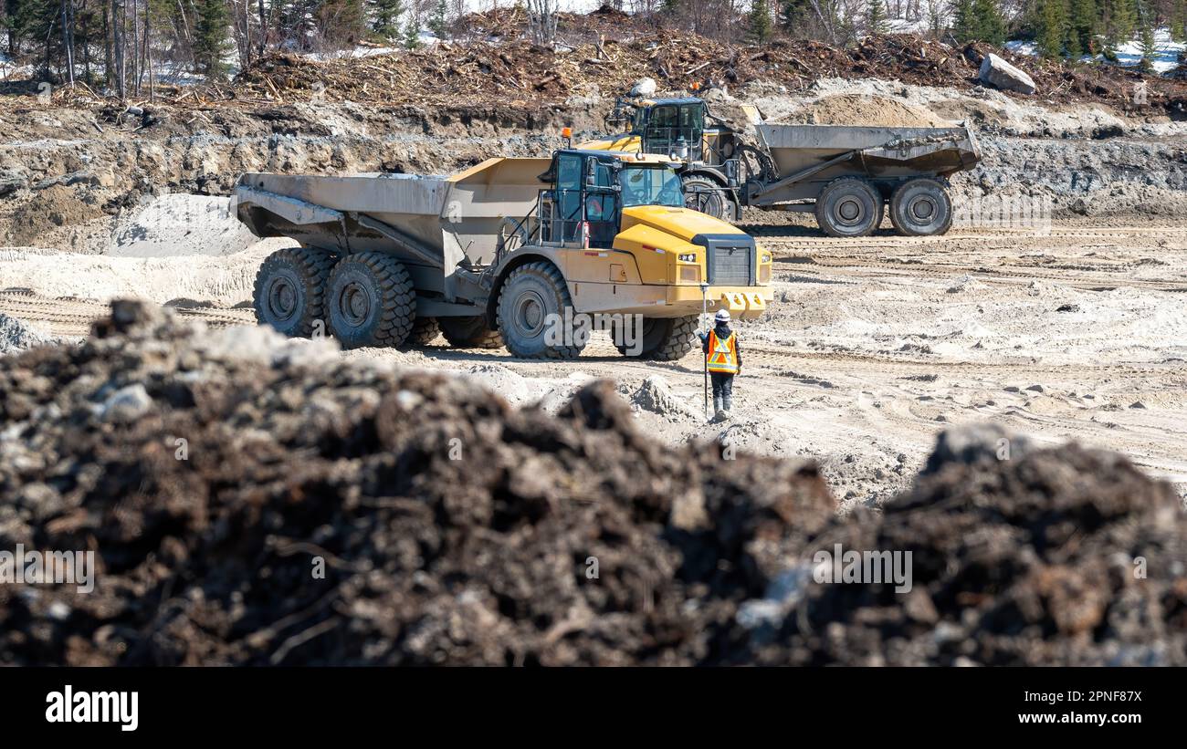 Dumpers driving on a construction site and a surveyor on a sunny day Stock Photo
