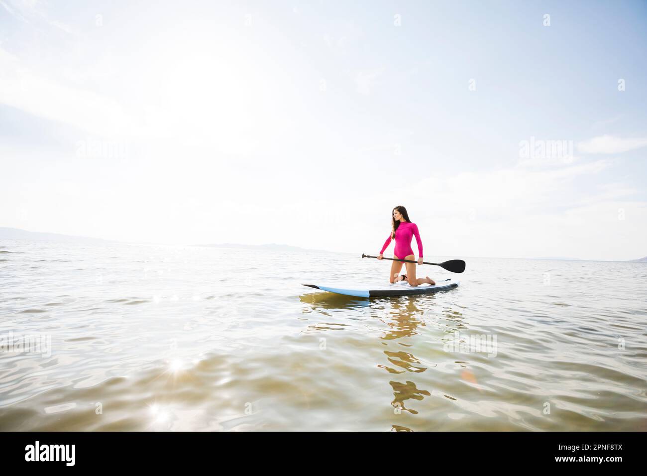 Woman kneeling on paddleboar in lake Stock Photo