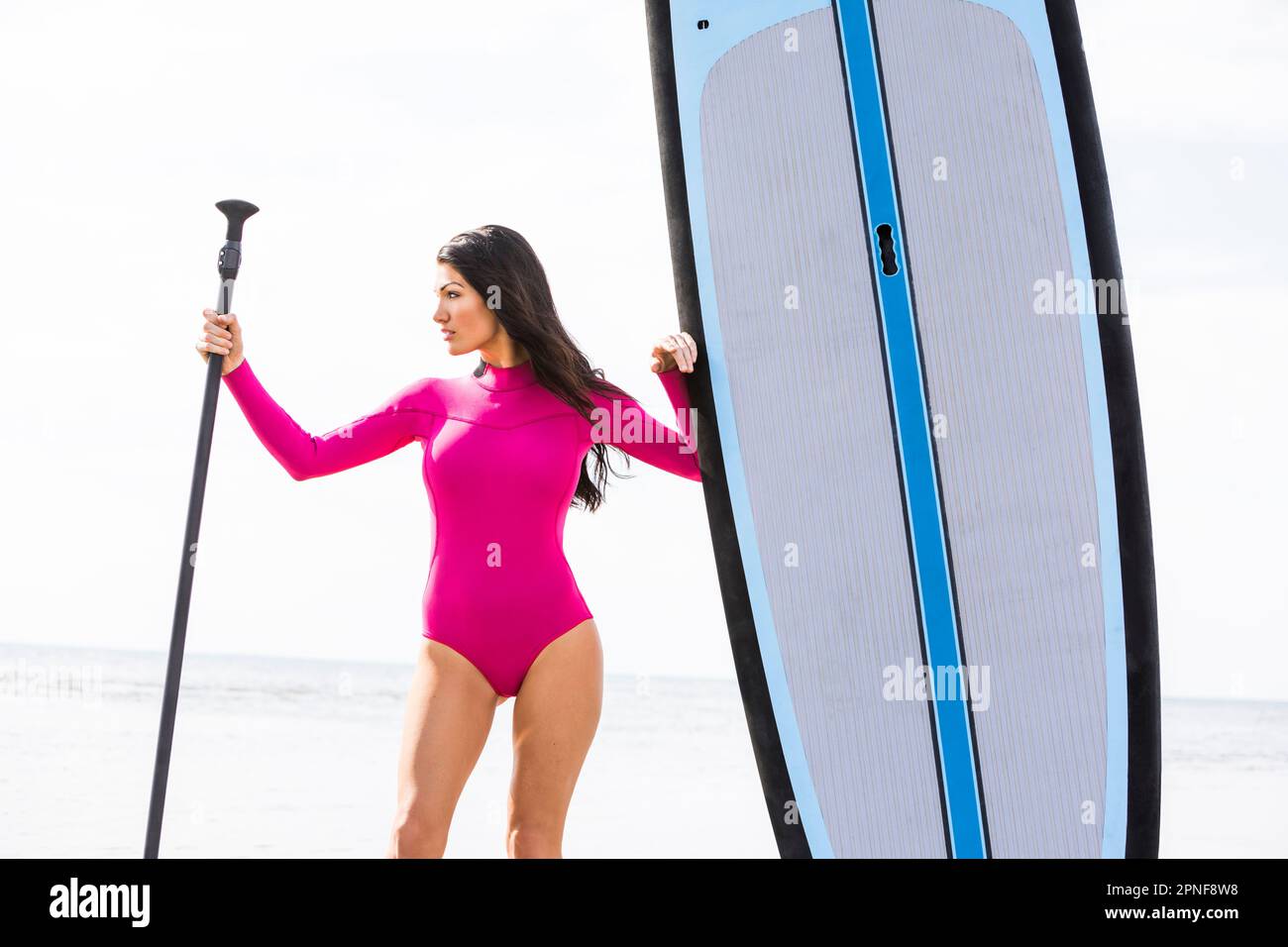 Woman holding oar next to paddleboard on beach Stock Photo
