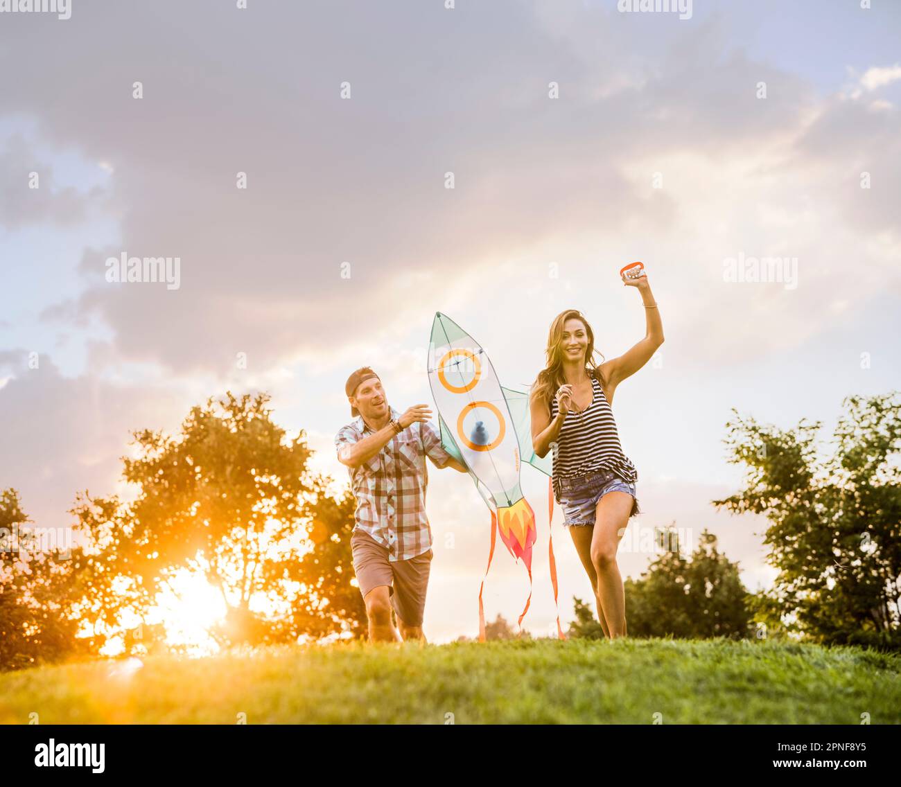 Woman and man running with kite in park at sunset Stock Photo