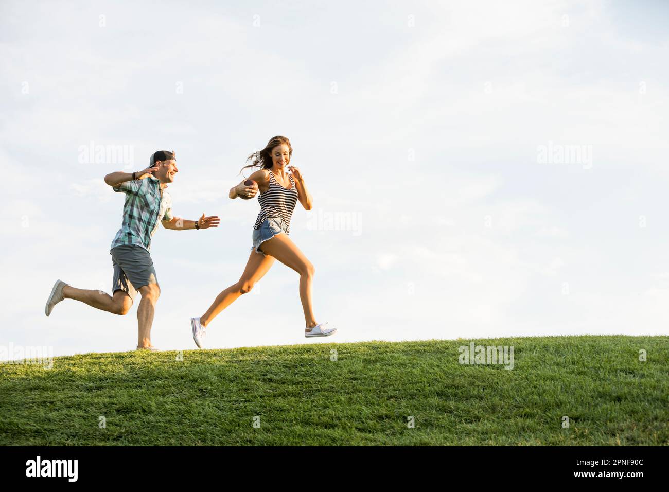 Woman and man running on grassy hill in park Stock Photo