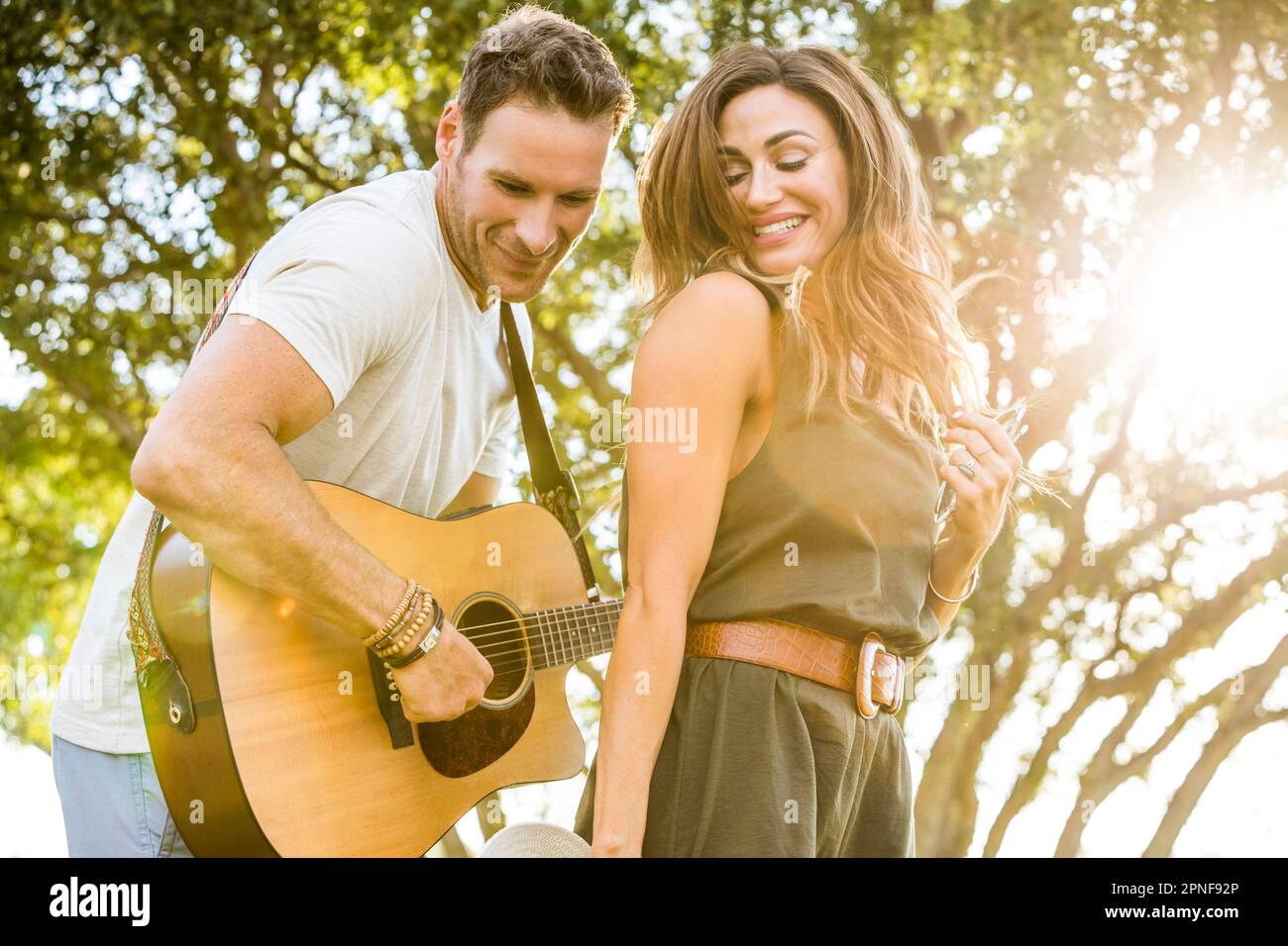 Woman dancing to music while man playing guitar in park Stock Photo