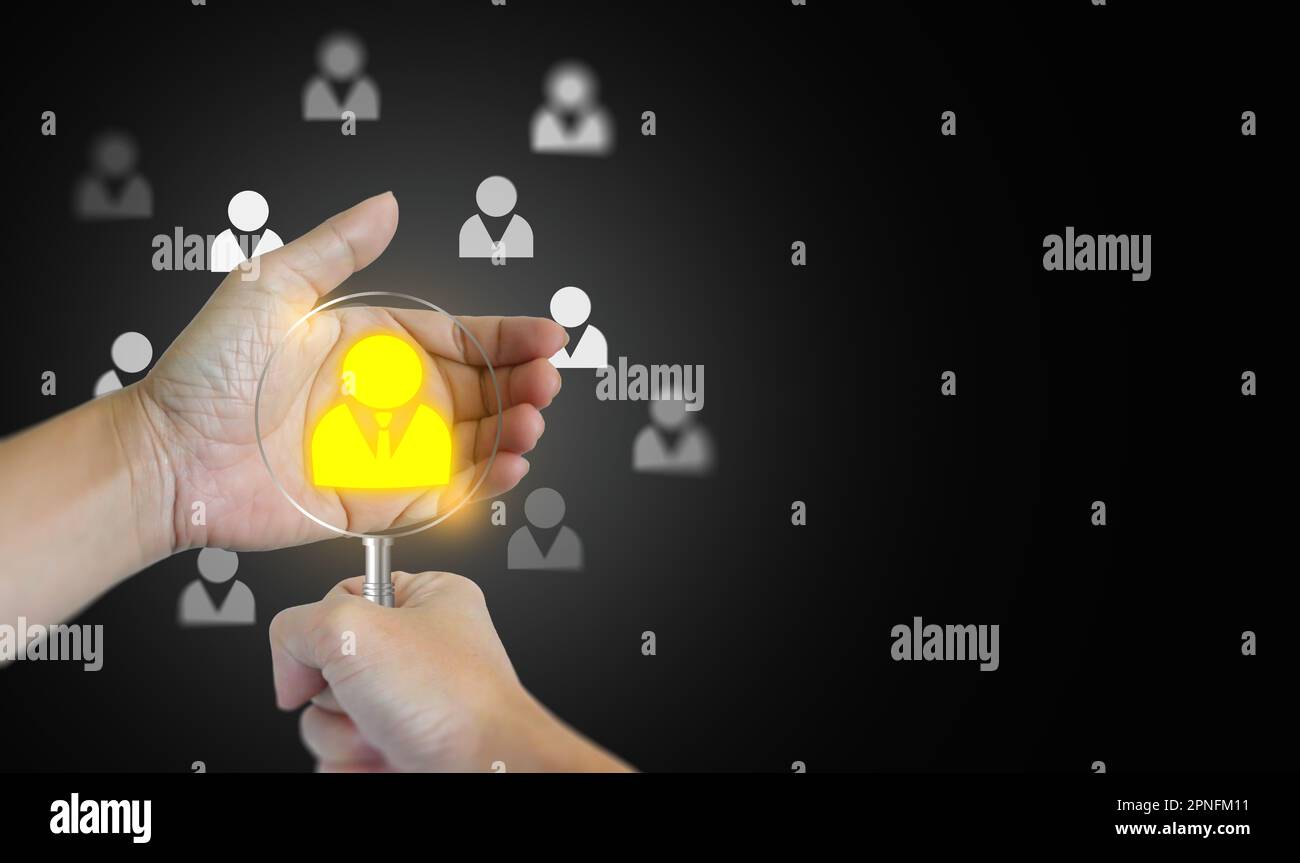 A hand with a magnifying glass and the other hand holding a found potential personnel icon among many others. HRM or Human Resource Management. Human Stock Photo