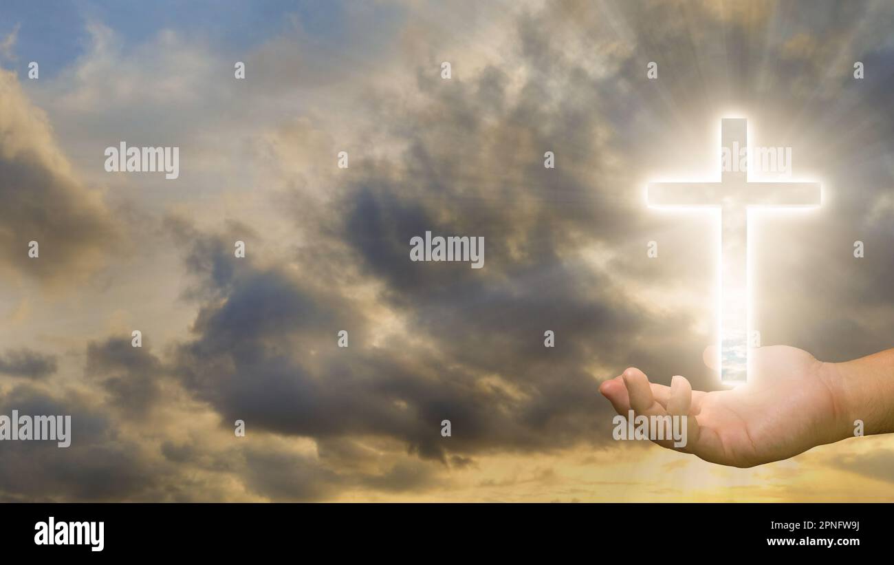Conceptual image of a Christian cross on a human hand over a sunset sky ...