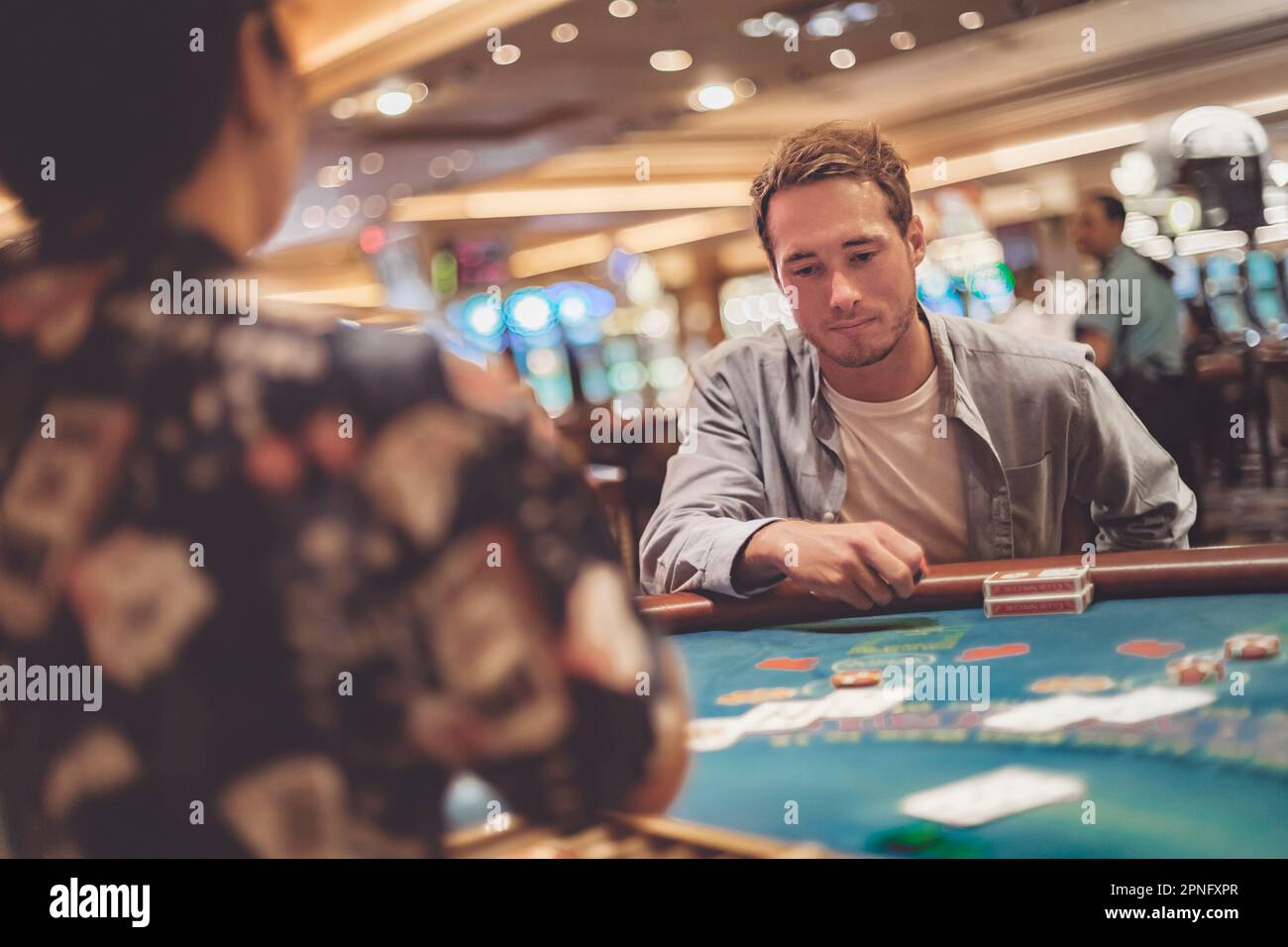 Casino gambling young man playing blackjack at table with cards and chips. Indoor portrait of gambler with dealer Stock Photo