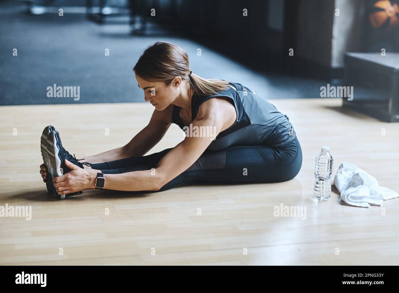 Premium Photo  Woman stretches her legs and warms up before having a  dumbbell workout in the gym with water bottle ready next to her.