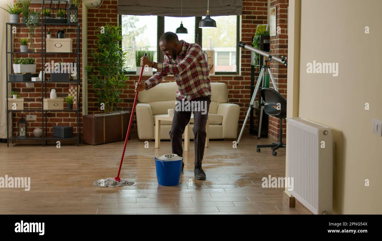 Cheerful boyfriend dancing and washing floors with all purpose cleaner