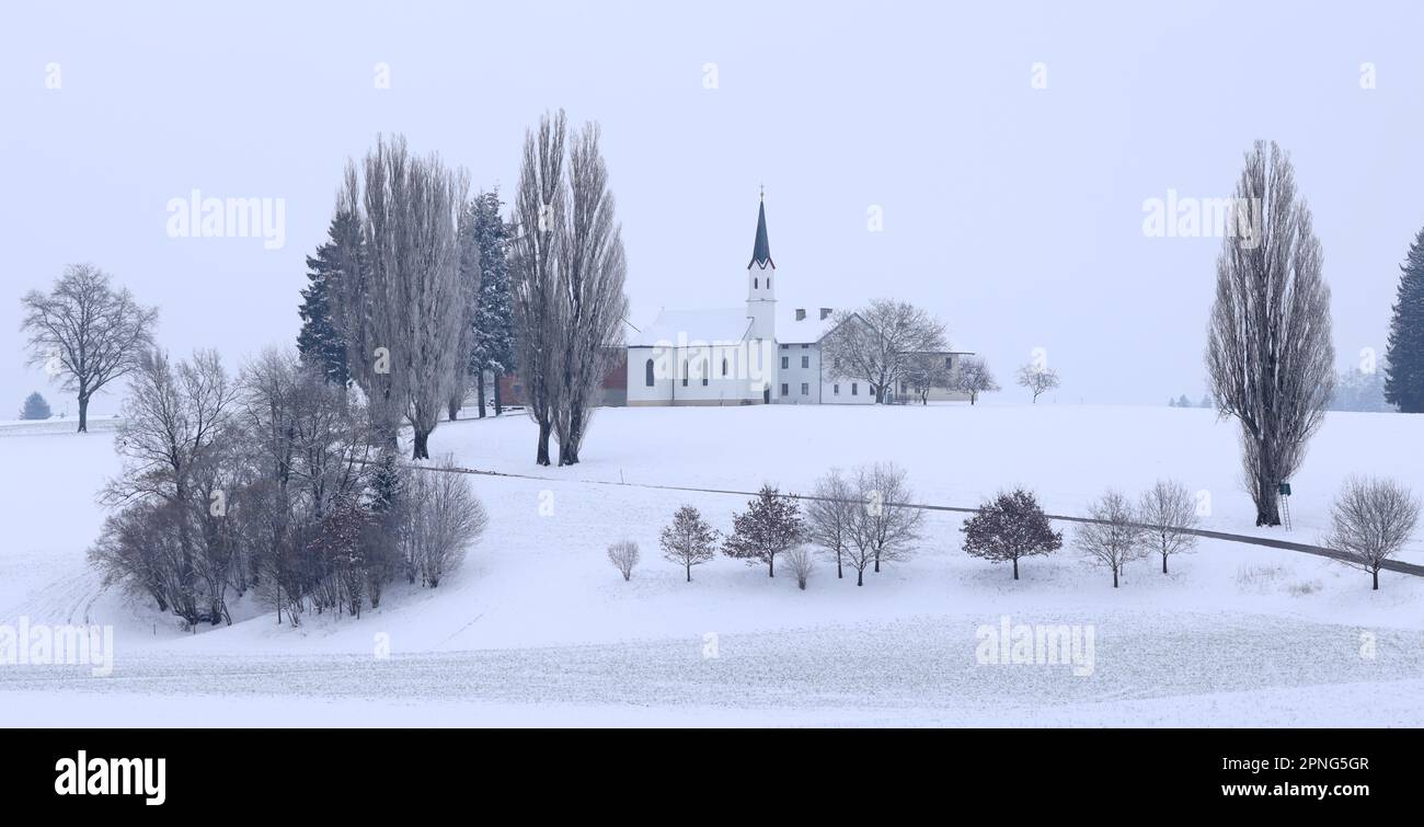 Small hamlet with chapel in snowy landscape in gloomy winter weather