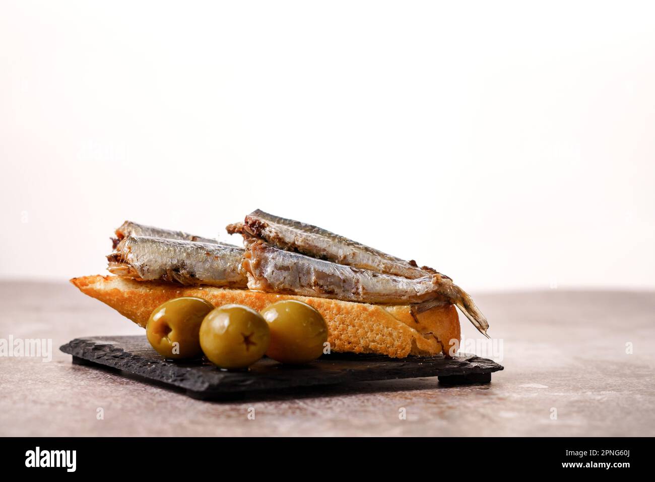 Tapa of sardines with tomato and olives on black slate and white