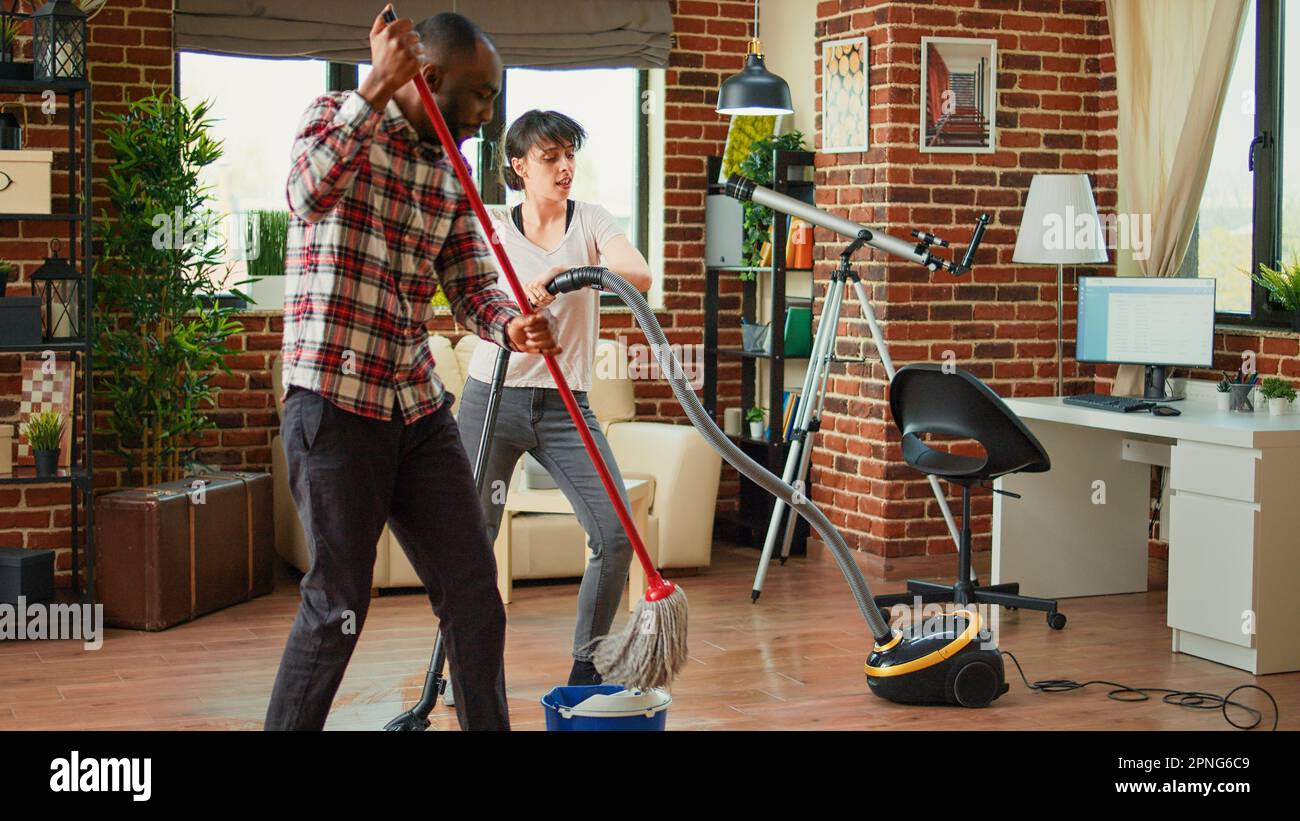 Young couple doing house chores and singing, listening to music for